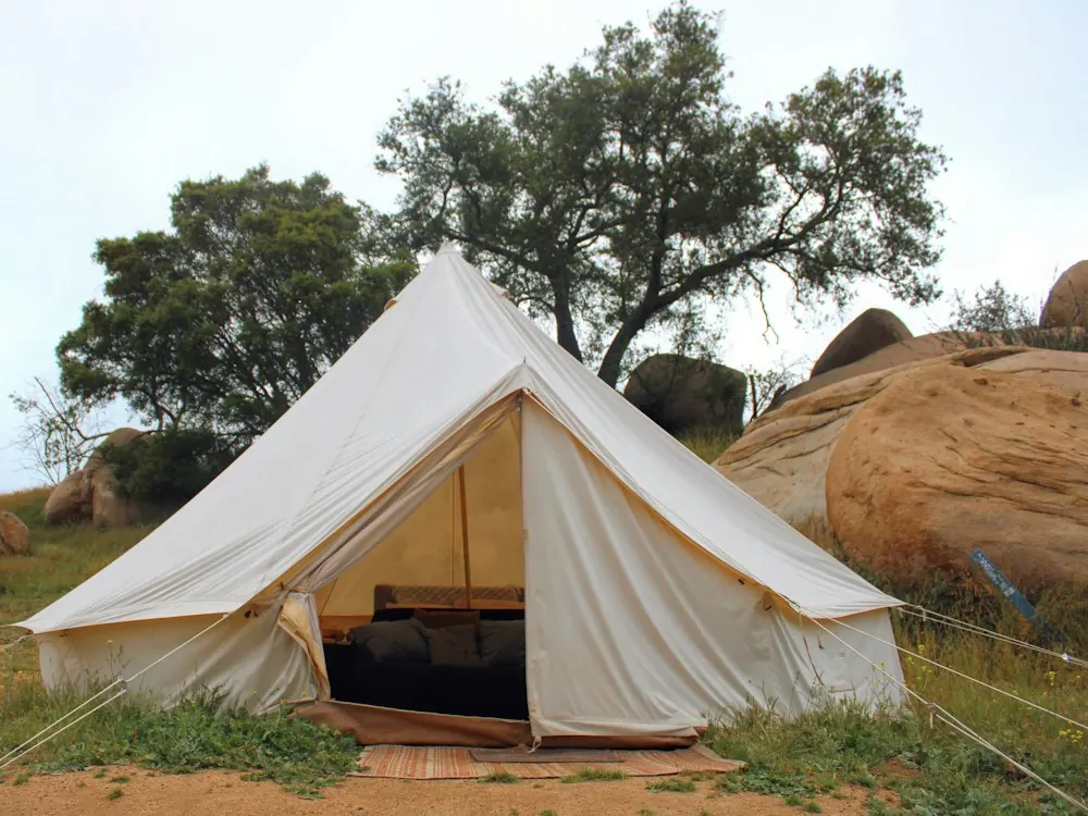 A canvas bell tent pitched among trees and boulders