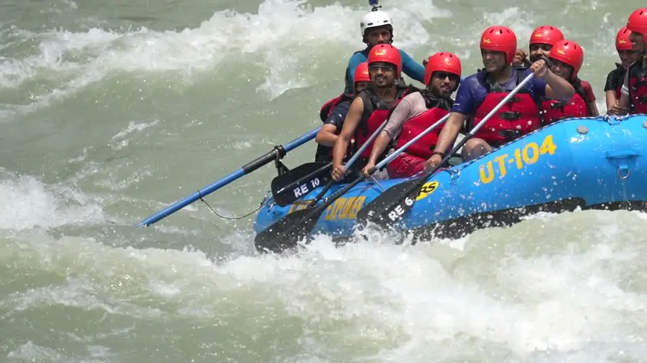A full raft of paddlers in red helmets and certified whitewater life jackets driving through whitewater on the Ganga near Rishikesh, with the lead guide visible at the front of the raft