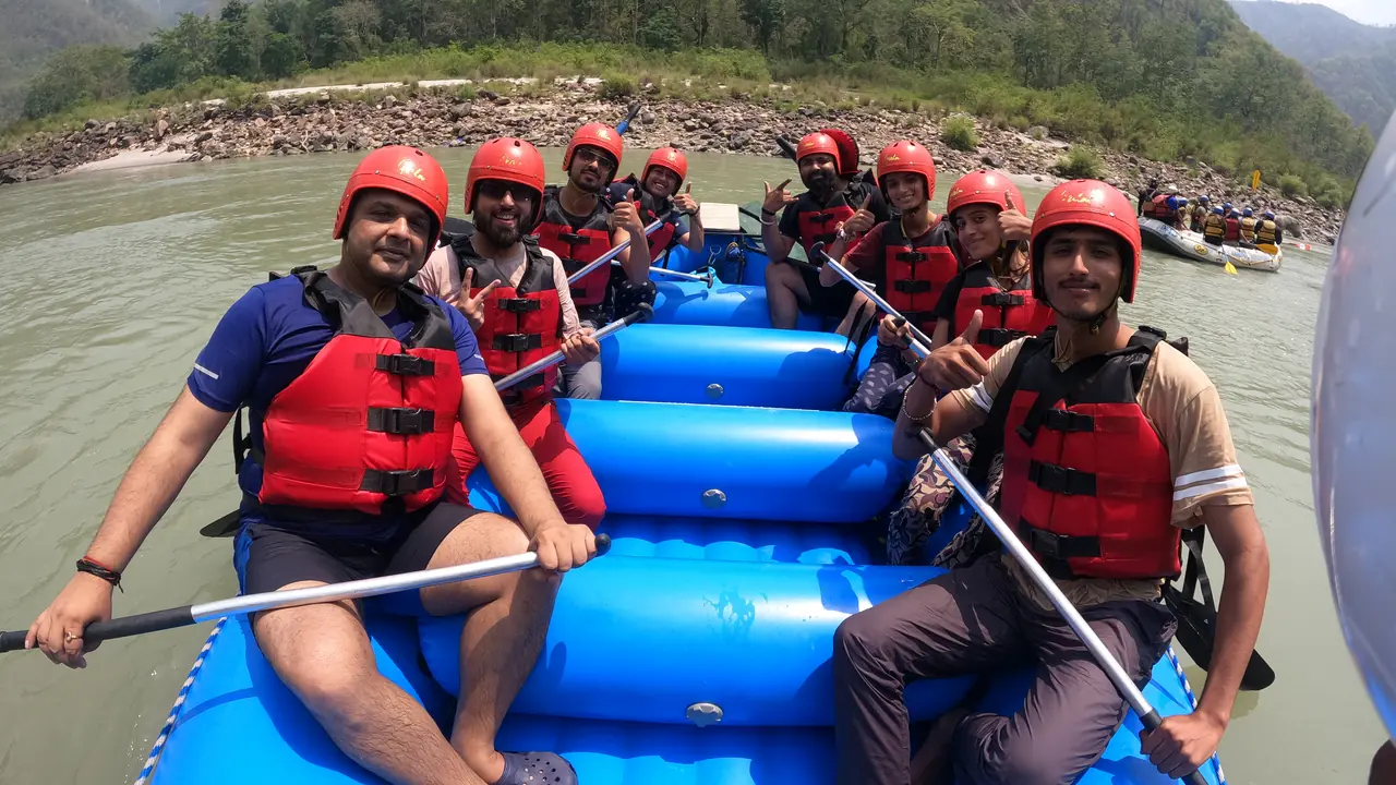 A full raft of rafters in red helmets and life jackets, paddles in hand, moving through the Ganga canyon near Rishikesh